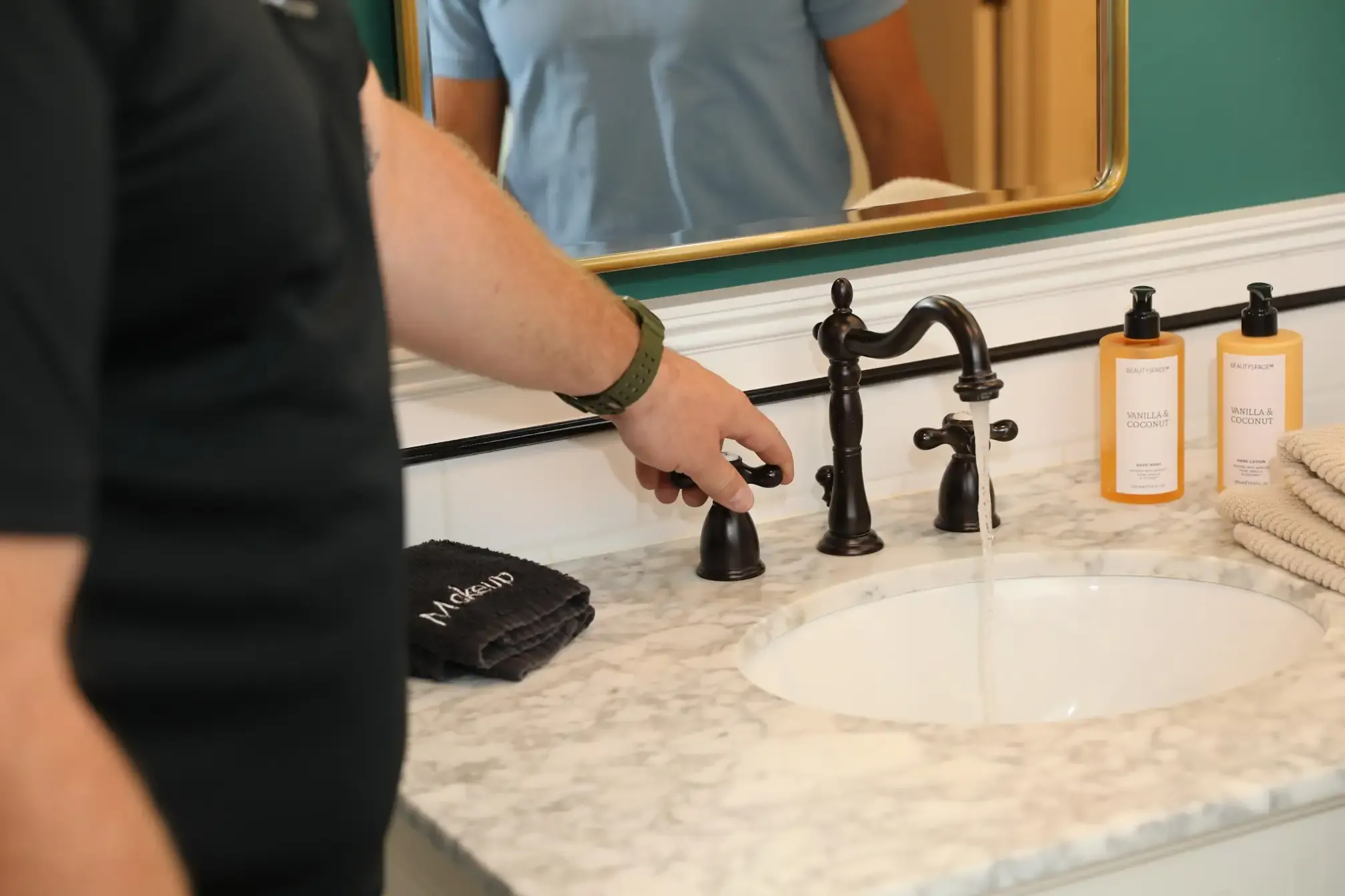 Plumber tests the water flow of a newly installed dark-finish widespread faucet in a clean residential bathroom.