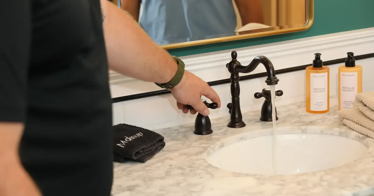 Plumber tests the water flow of a newly installed dark-finish widespread faucet in a clean residential bathroom.