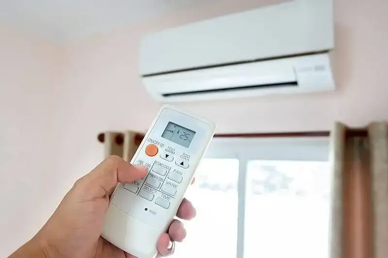 Hand holding a remote control aimed at a wall-mounted air conditioner.