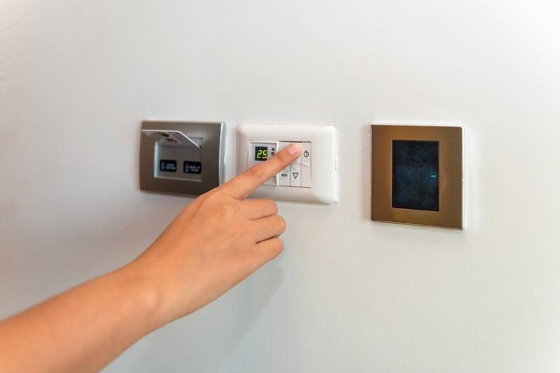 Homeowner adjusting a modern digital thermostat for temperature control.
