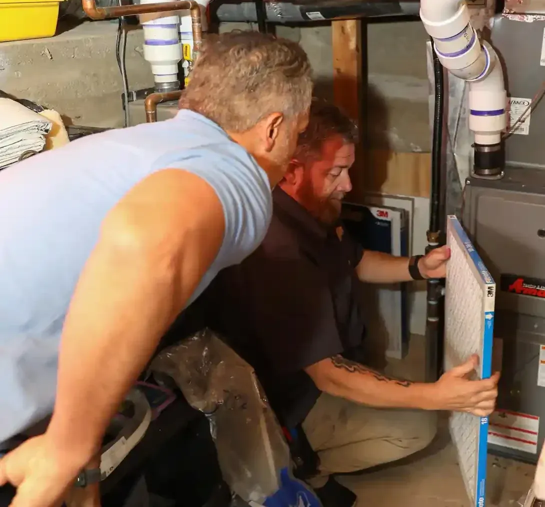 Technician putting back a cleaned furnace air filter to a Lennox furnace unit in a basement.
