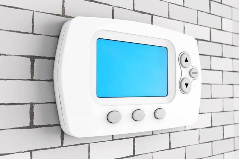 Digital thermostat with a blue screen and three buttons displayed on a brick-patterned wall.