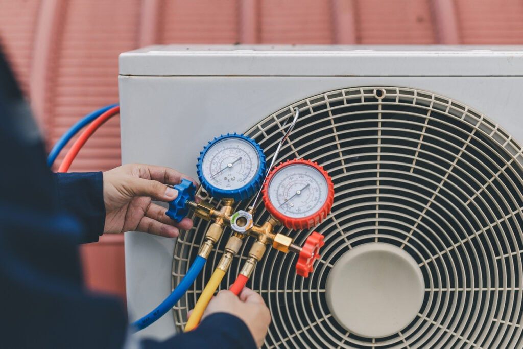 Hands adjusting pressure with gauges connected to an air conditioner unit.