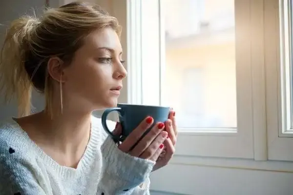 A woman sits with a cup by a window.
