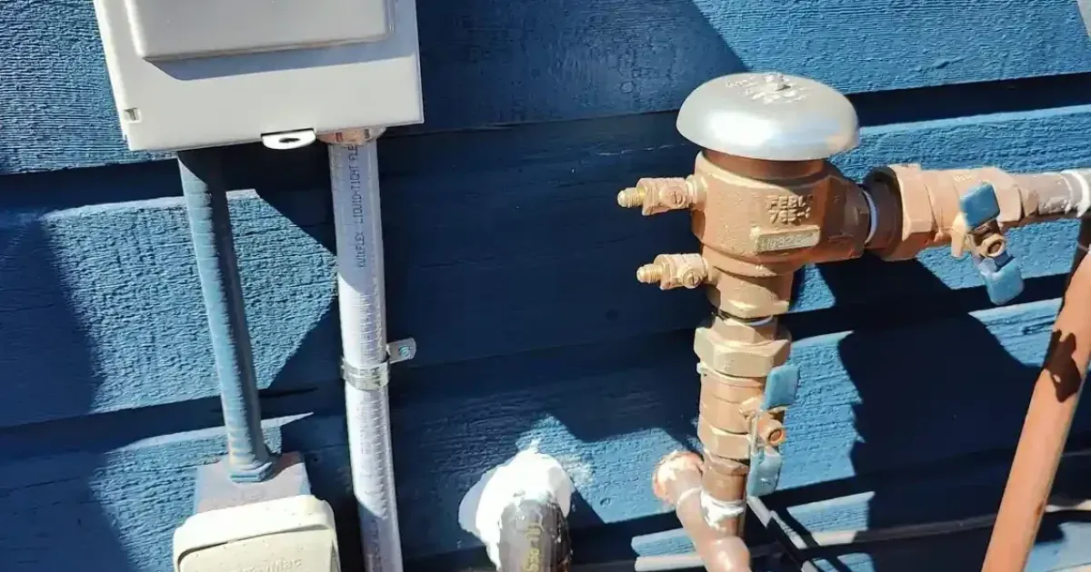 A Febco pressure vacuum breaker backflow preventer installed on an exterior wall for an irrigation system.