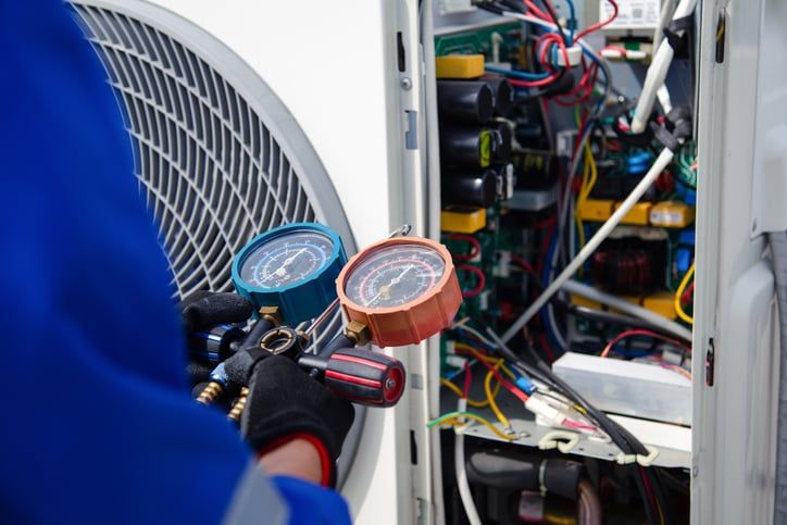 Technician measuring pressure with gauges, examining an open air conditioning unit.