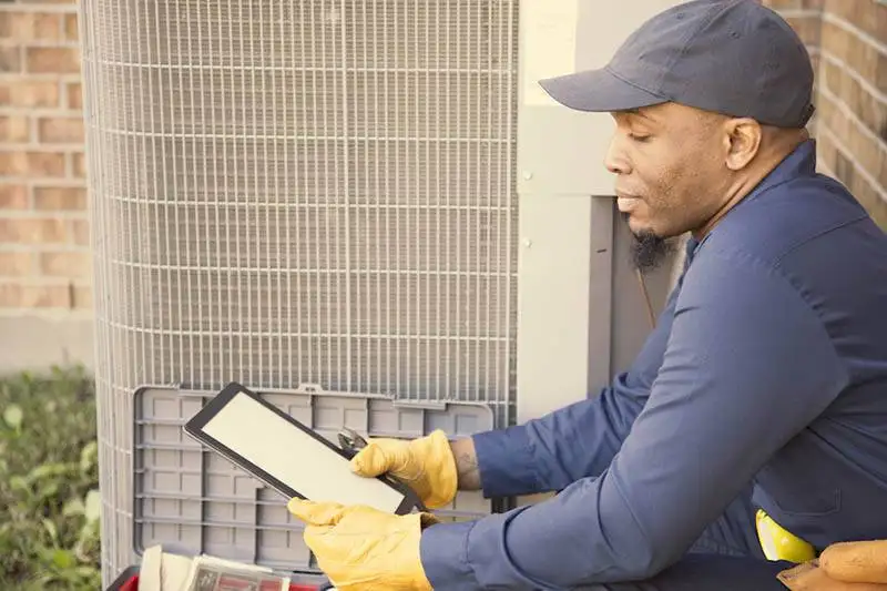 HVAC technician uses a tablet while inspecting an outdoor HVAC unit in a Colorado home.
