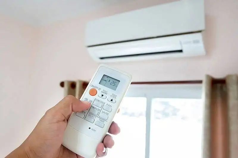 Hand holding a remote control aimed at a wall-mounted air conditioner.