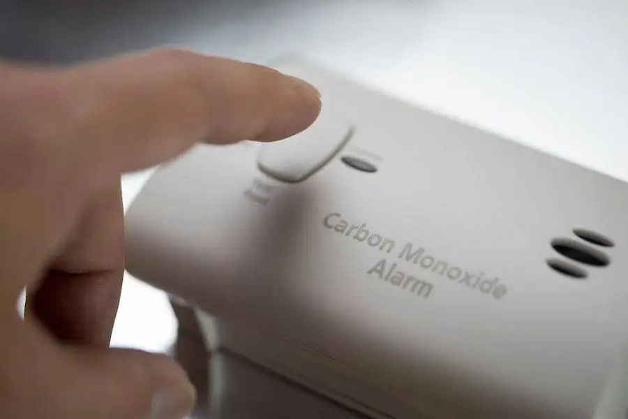 Hand pressing alarm button on a white carbon monoxide alarm.