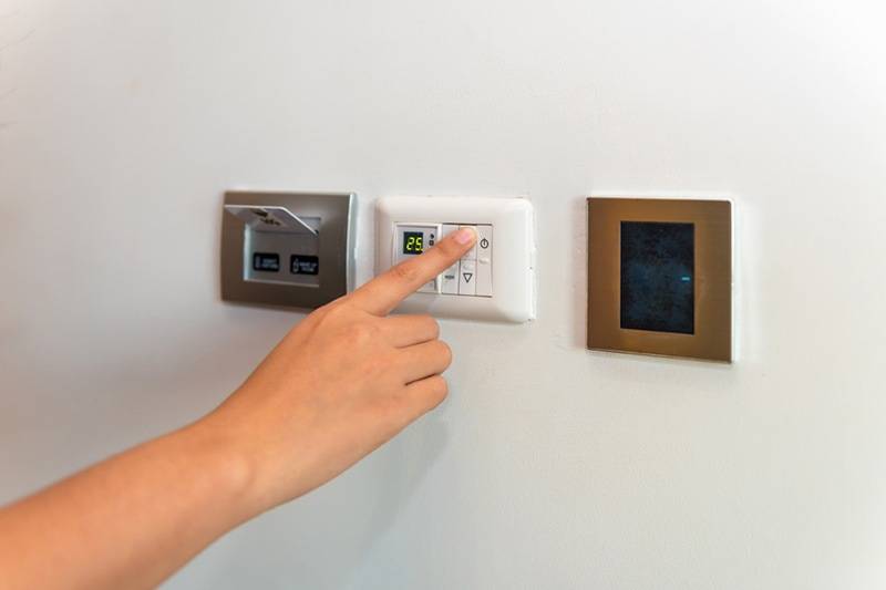 Homeowner adjusting a modern digital thermostat for temperature control.
