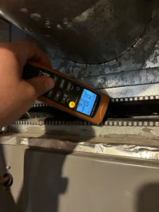 Technician taking a carbon monoxide reading with a handheld CO meter above the furnace during AC system repair in Loveland, CO