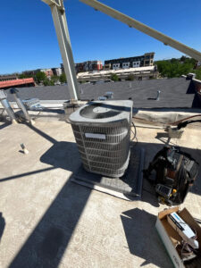 Fort Collins AC repair technician replacing an outdoor fan motor and capacitor on a rooftop condenser unit to restore cooling