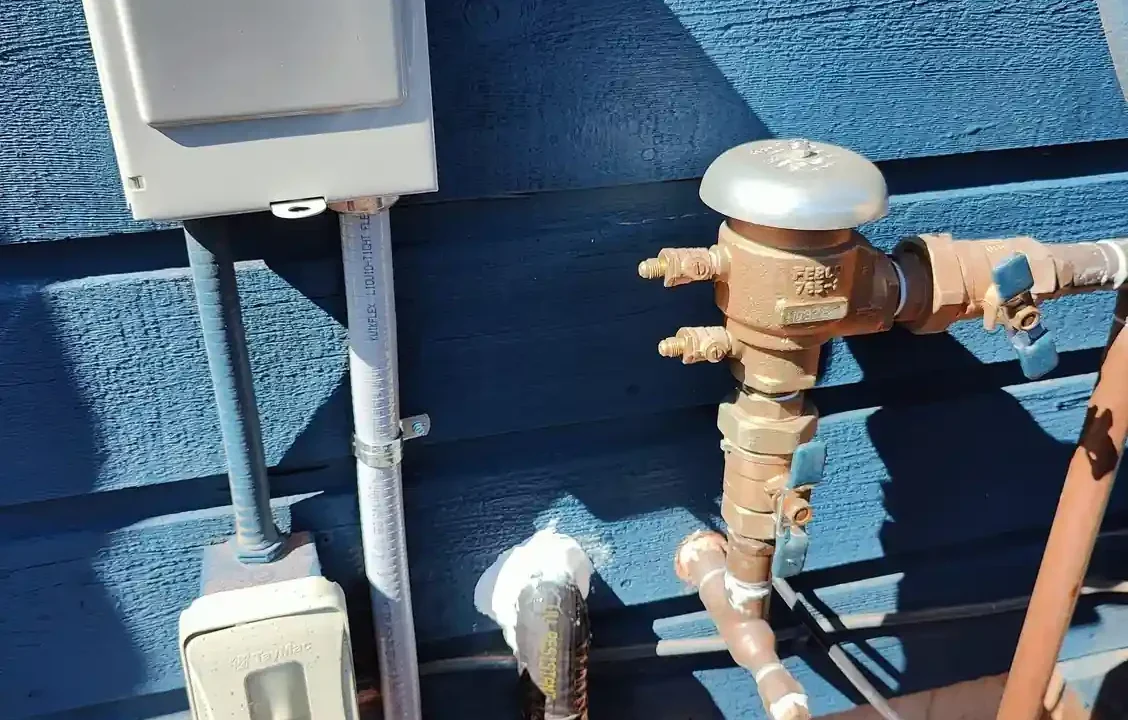 A Febco pressure vacuum breaker backflow preventer installed on an exterior wall for an irrigation system.