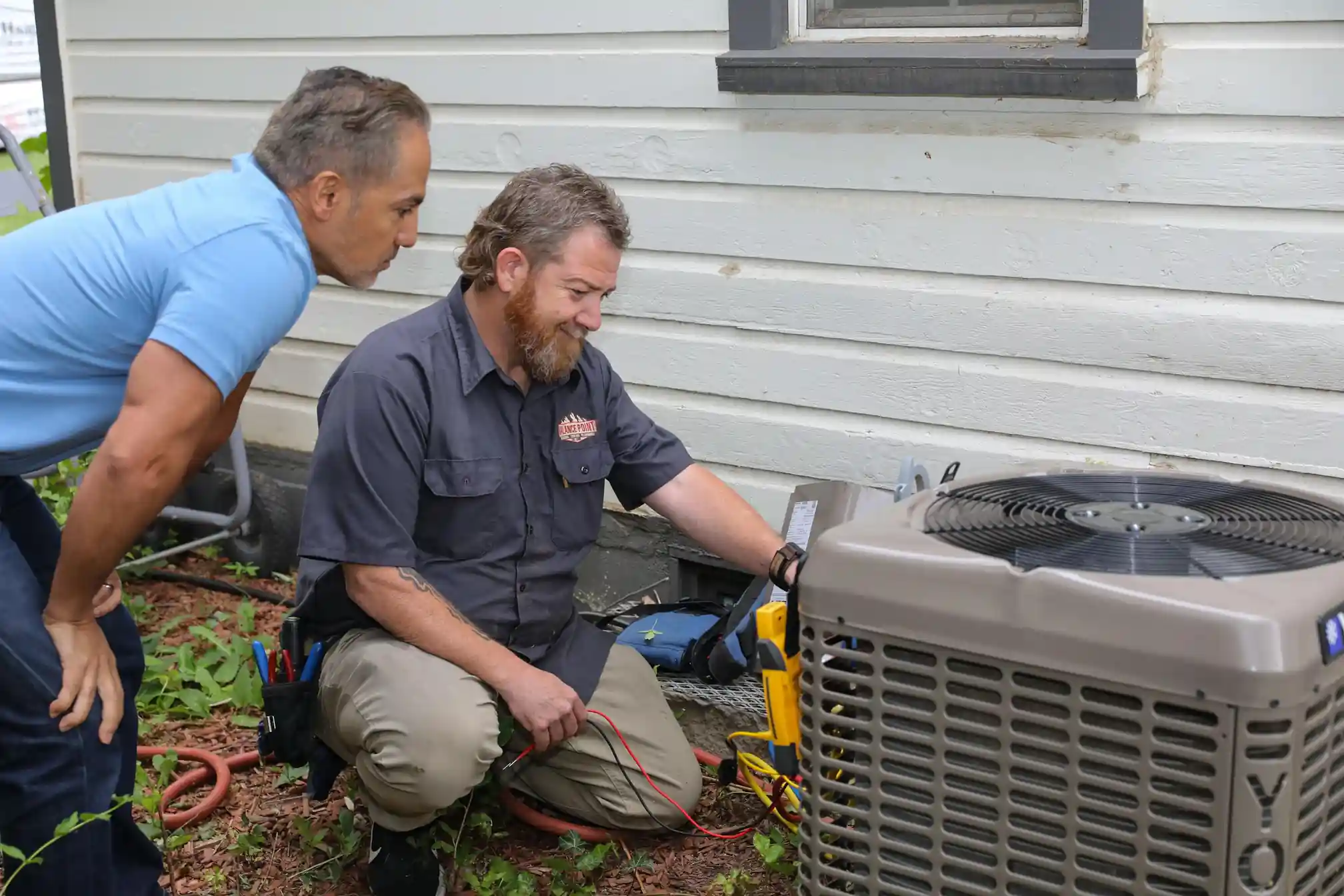HVAC technician in uniform, diagnosing electrical issues within an outdoor York AC unit after installation.