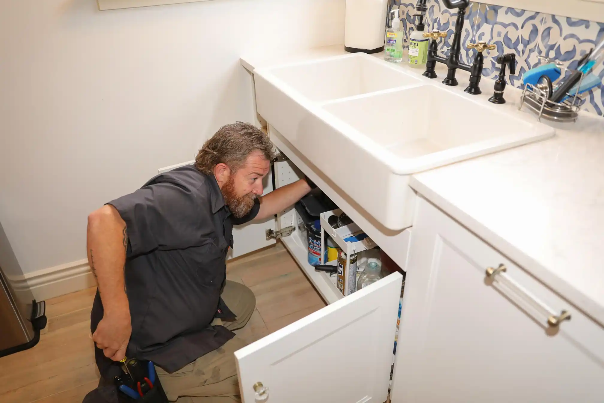 Plumber accesses the cabinet under a stylish kitchen sink to perform focused repair or maintenance work on the pipes.