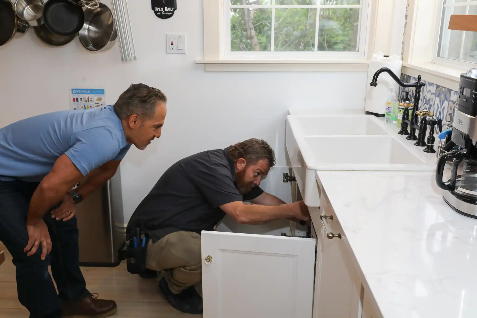 Plumber works under a kitchen sink in a modern home, performing focused repair or maintenance activities.