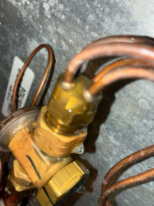 Fort Collins AC repair technician inspecting refrigerant lines and expansion valve during a nitrogen pressure leak search to restore cooling