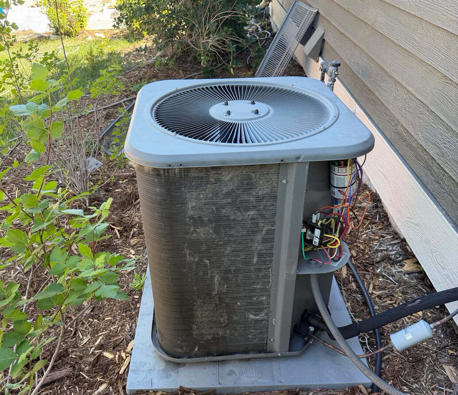 Dirty AC condenser unit with buildup on the coils outside a Fort Collins home served by Balance Point Heating, Cooling & Plumbing