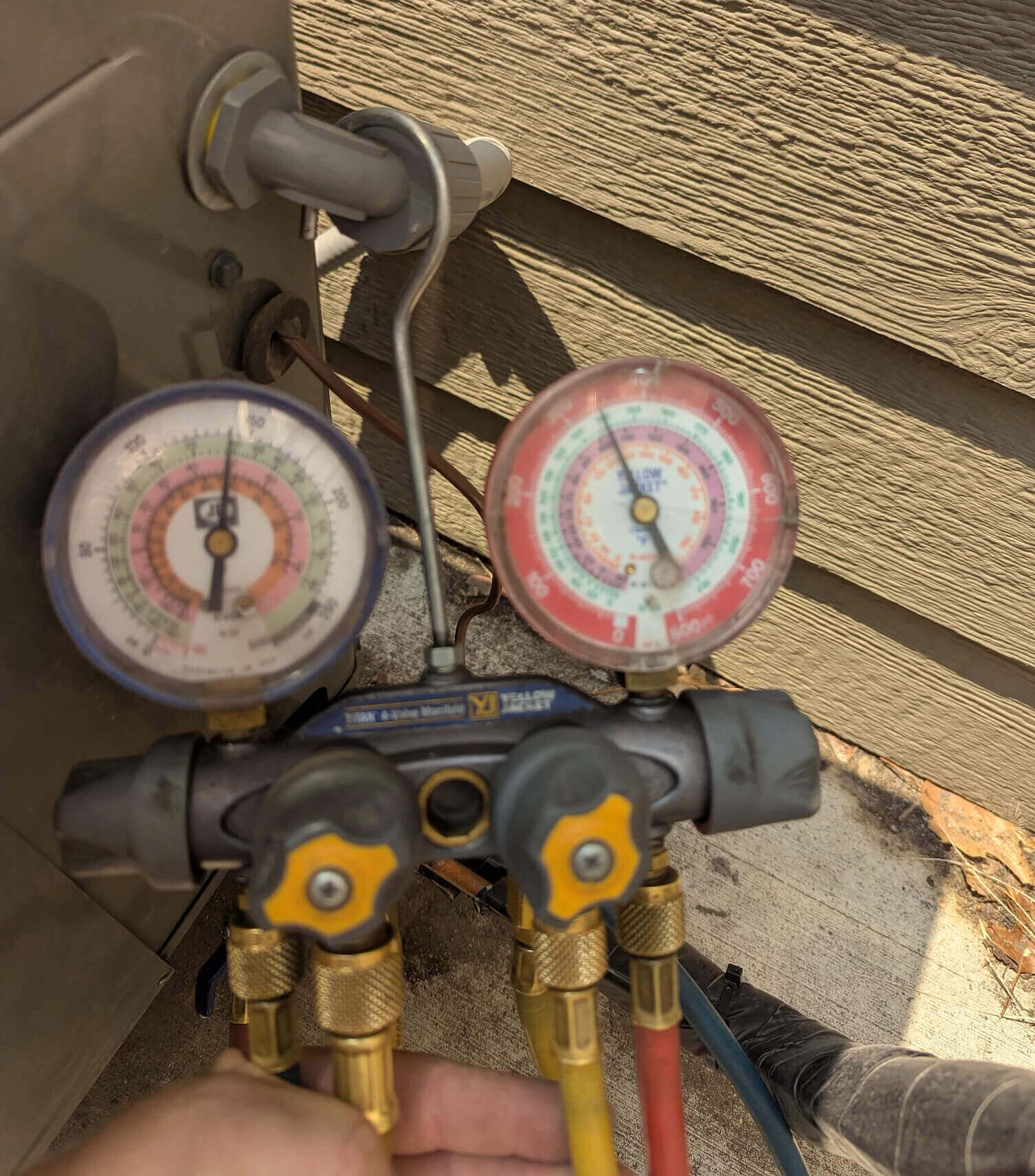 Technician checking AC refrigerant pressure with manifold gauges outside a Fort Collins home served by Balance Point Heating, Cooling & Plumbing