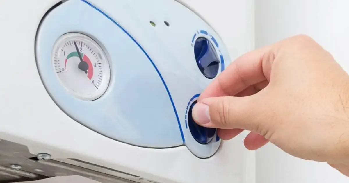 Person adjusting control knob on a wall-mounted water heater.