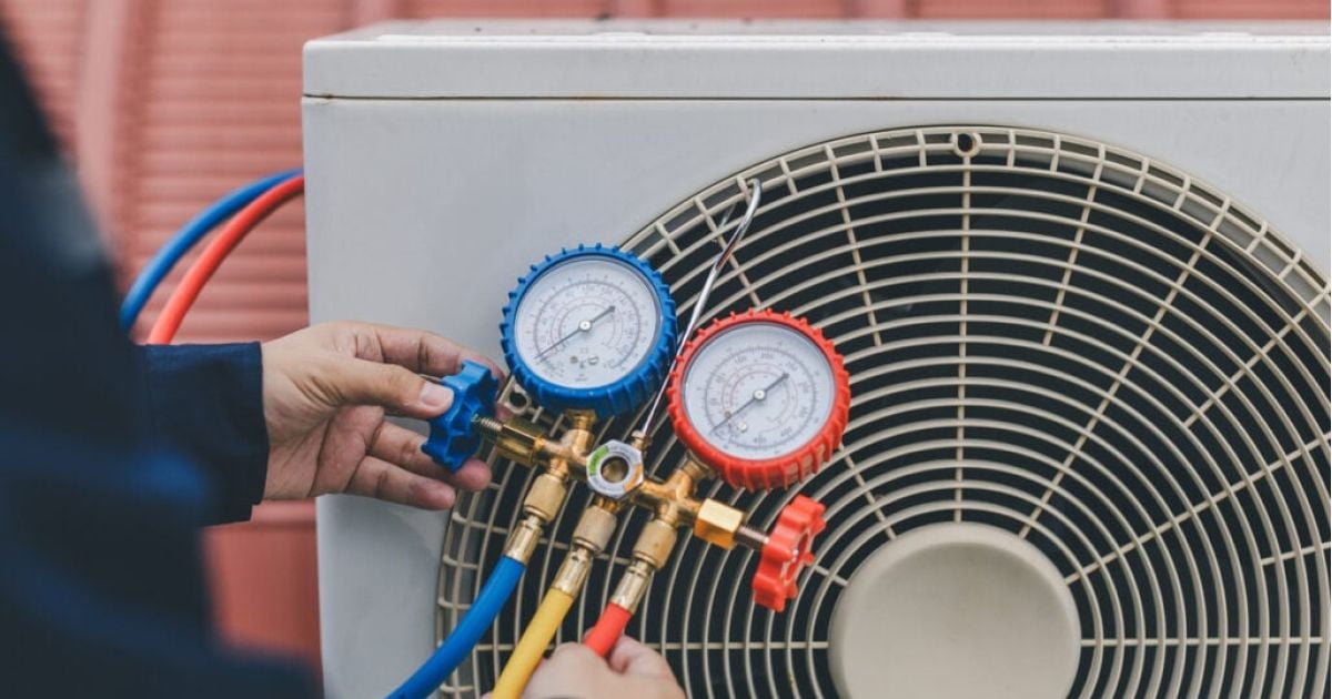 Hands adjusting pressure with gauges connected to an air conditioner unit.