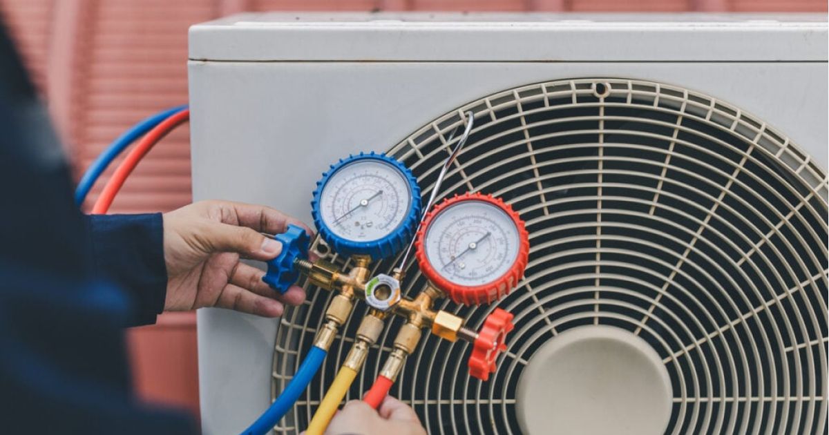 Hands adjusting pressure with gauges connected to an air conditioner unit.