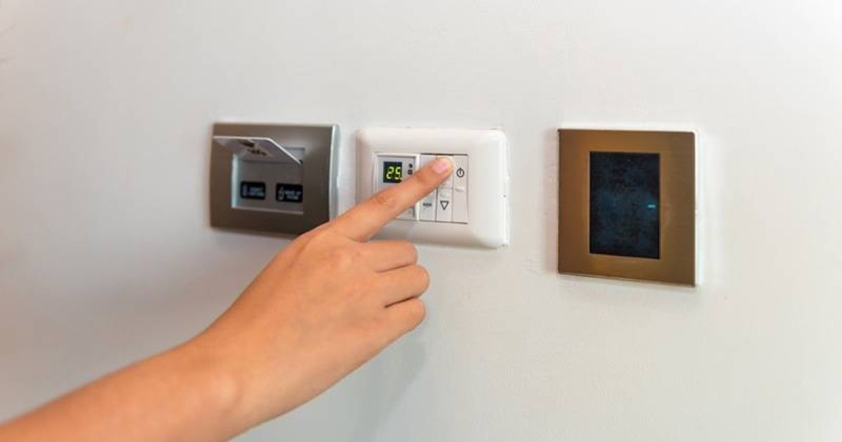Homeowner adjusting a modern digital thermostat for temperature control.
