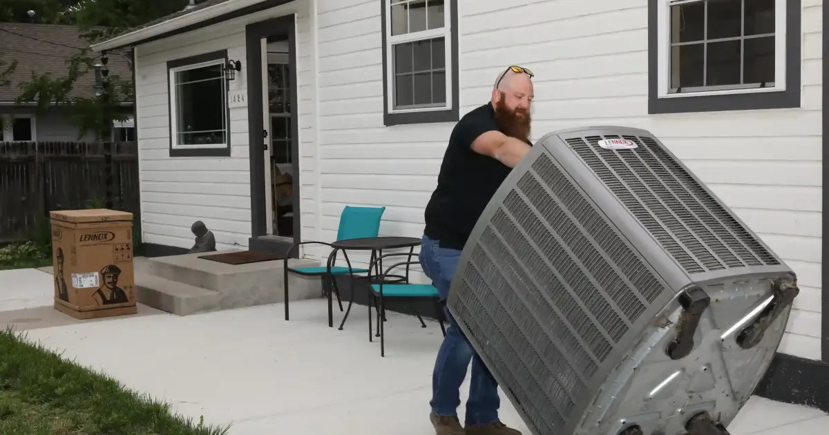 HVAC technician uses a hand truck to carefully move a new Lennox unit into a residential yard.