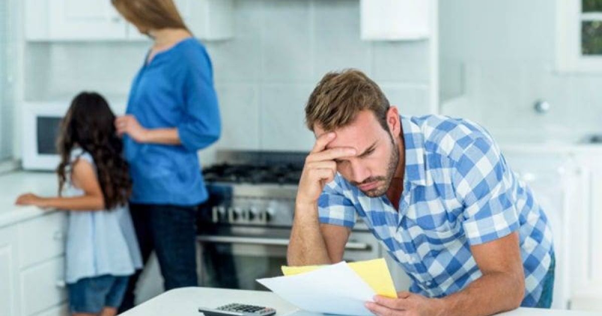 Worried father looking at bills with family in background.