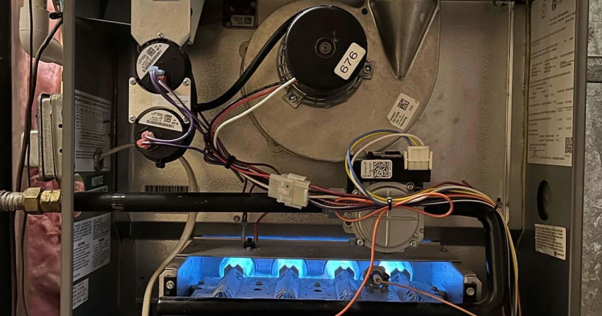 Open furnace cabinet showing blue burner flames and blower motor during a service call in a Fort Collins home served by Balance Point Heating, Cooling & Plumbing