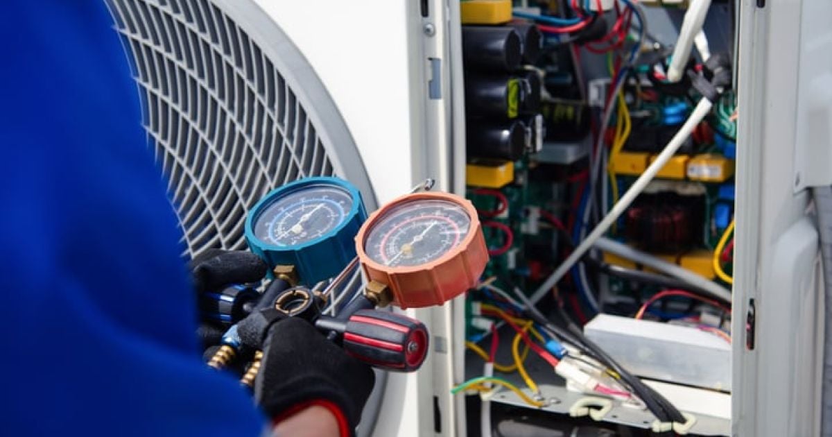 Technician measuring pressure with gauges, examining an open air conditioning unit.