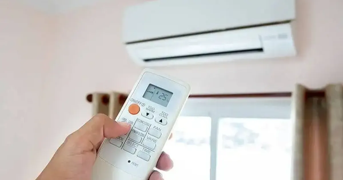 Hand holding a remote control aimed at a wall-mounted air conditioner.